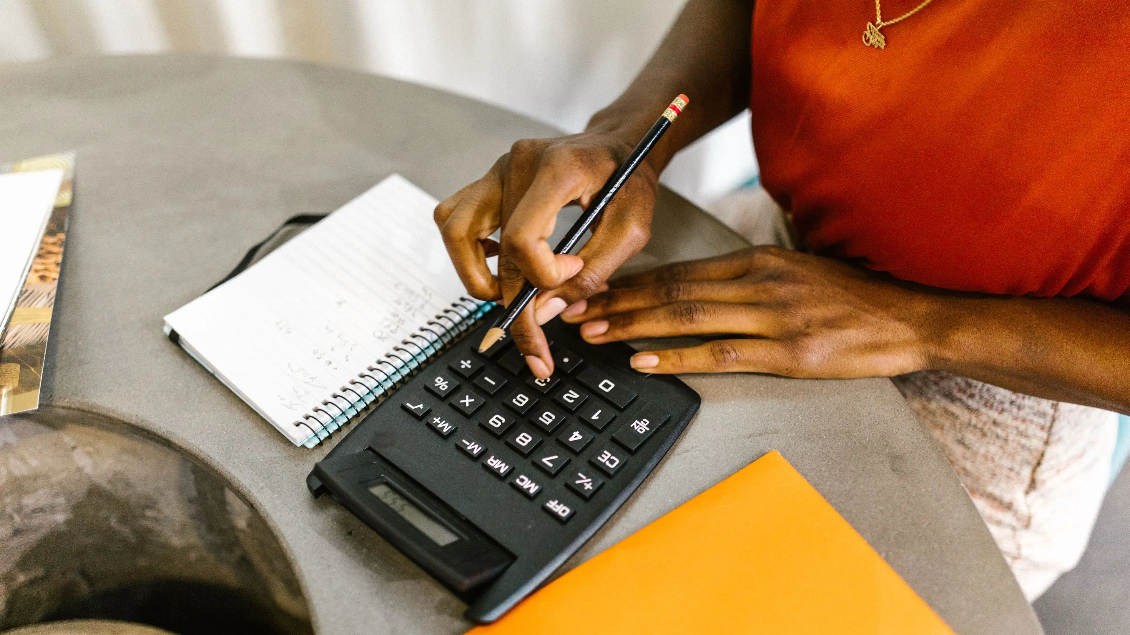 Hands working a calculator next to a handwritten spiral notebook